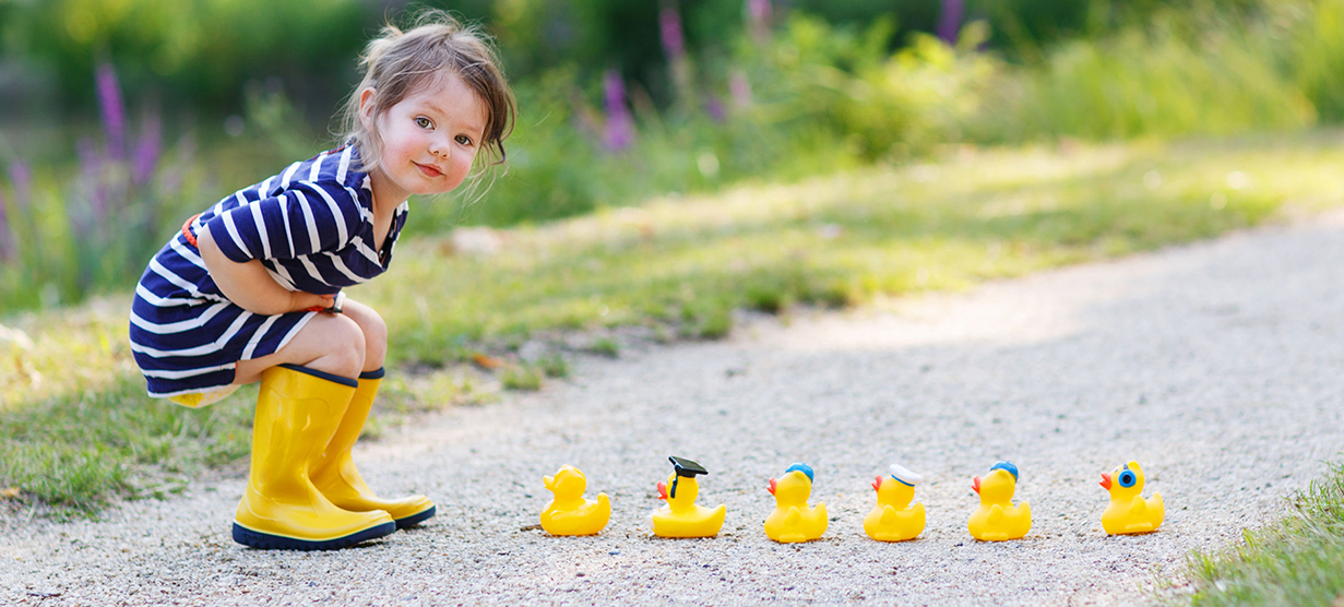 adorable little girl of 2 playing with yellow rubber ducks in summer park.
